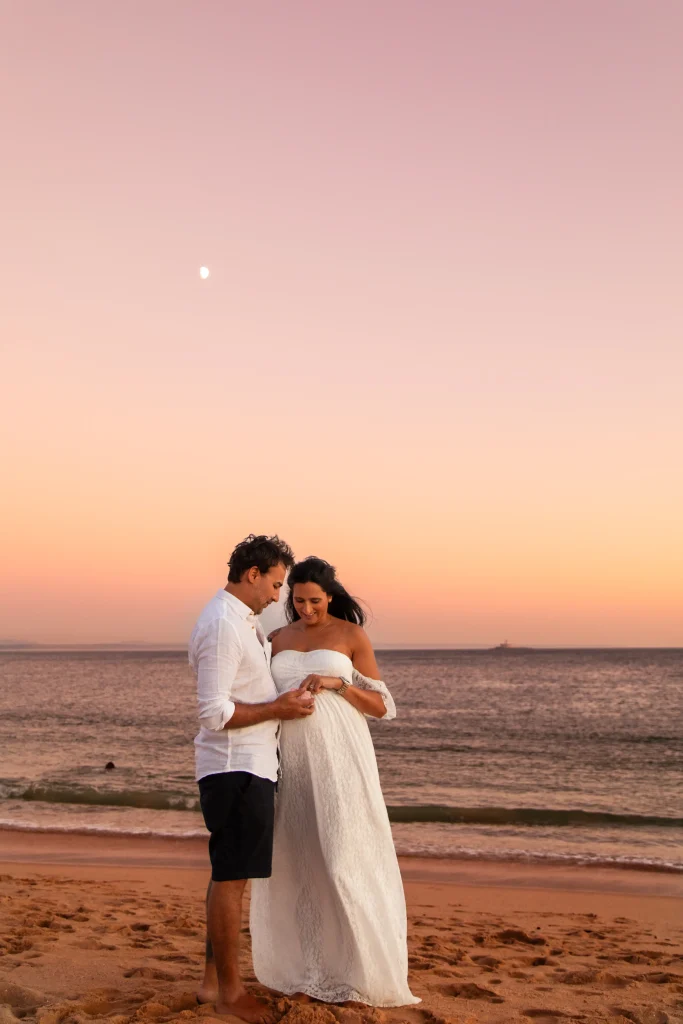 Pregnant couple embracing on the beach at sunset